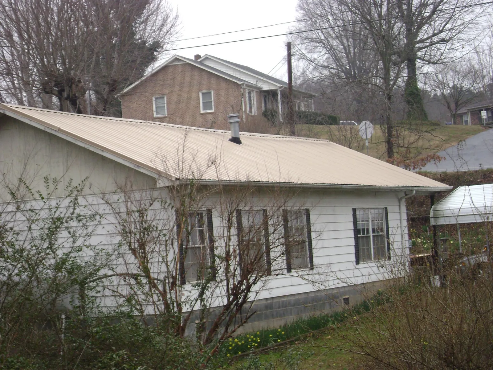 Tan metal roof on a white sided house set into a hillside — Commercial Roofing by Roofing Brothers in Cardiff By The Sea